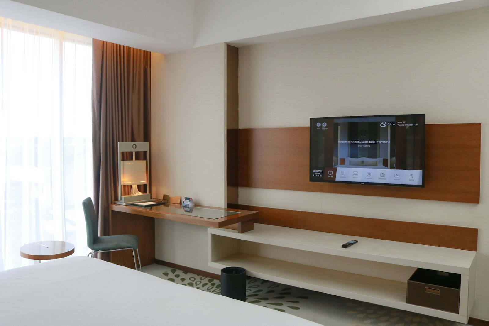 A hotel room with a wall-mounted TV and desk